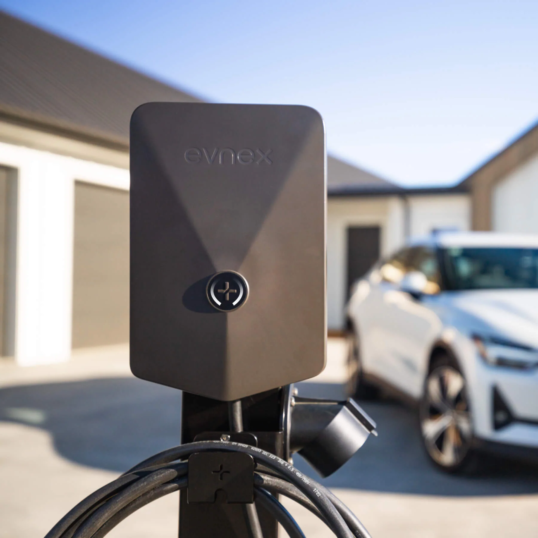 Evnex E2 Flex EV charger mounted on an outdoor post with a white electric vehicle in the background.